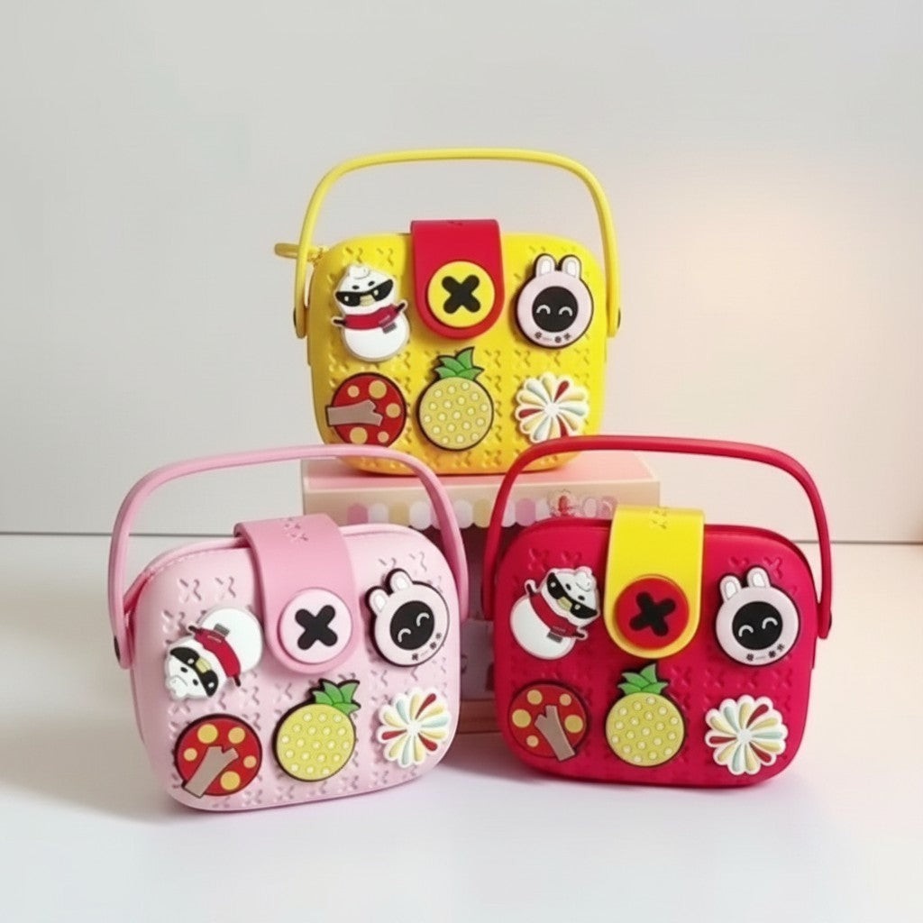 Mango Muffins Signature Series Charmer Sling crossbody bag for kids in pink, yellow, and red. Features EVA material, customizable charms, and a snap flap closure.