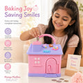 Mango Muffins Dream Cottage Savings Bank in candy pink and pastel blue with 3D charms, held by a smiling young girl.