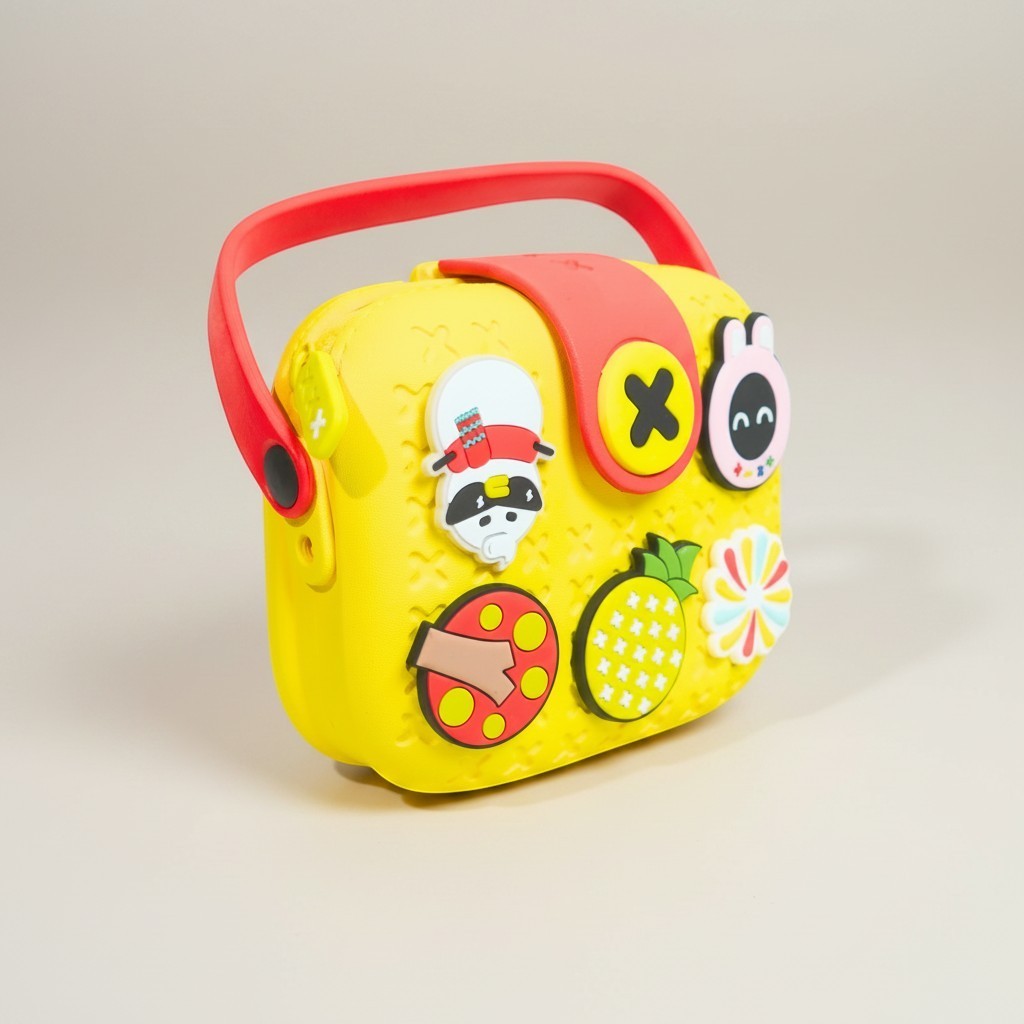 Mango Muffins yellow EVA sling bag for kids with red handle and colorful charms like a pineapple and bunny.